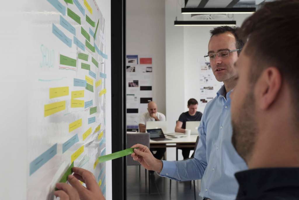 Two team members work together to sort feature cards on a wall as part of a research project