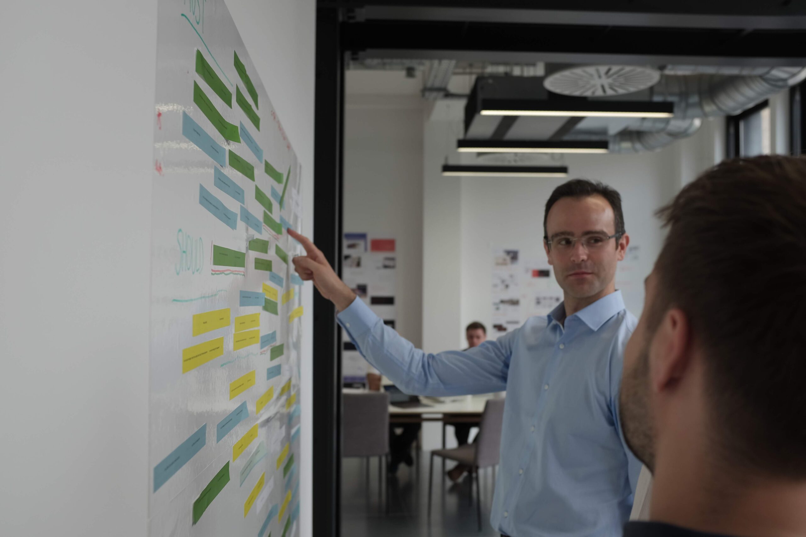 Two people order product feature cards on a wall as part of a digital project research exercise