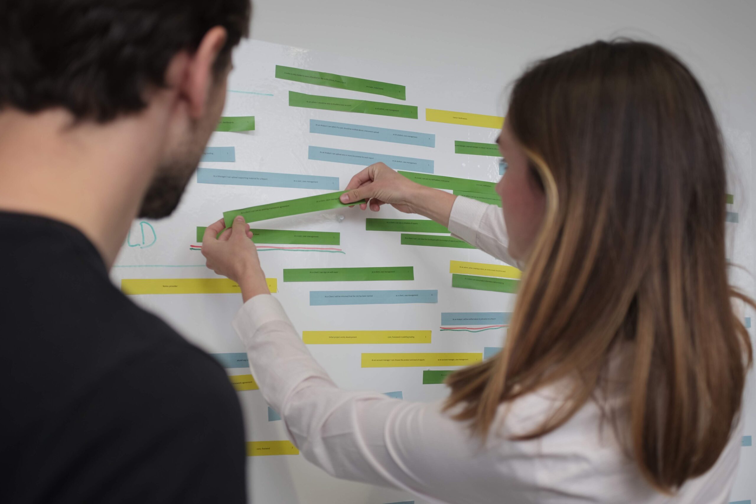 Two people stick feature ideas to a wall as part of a research exercise