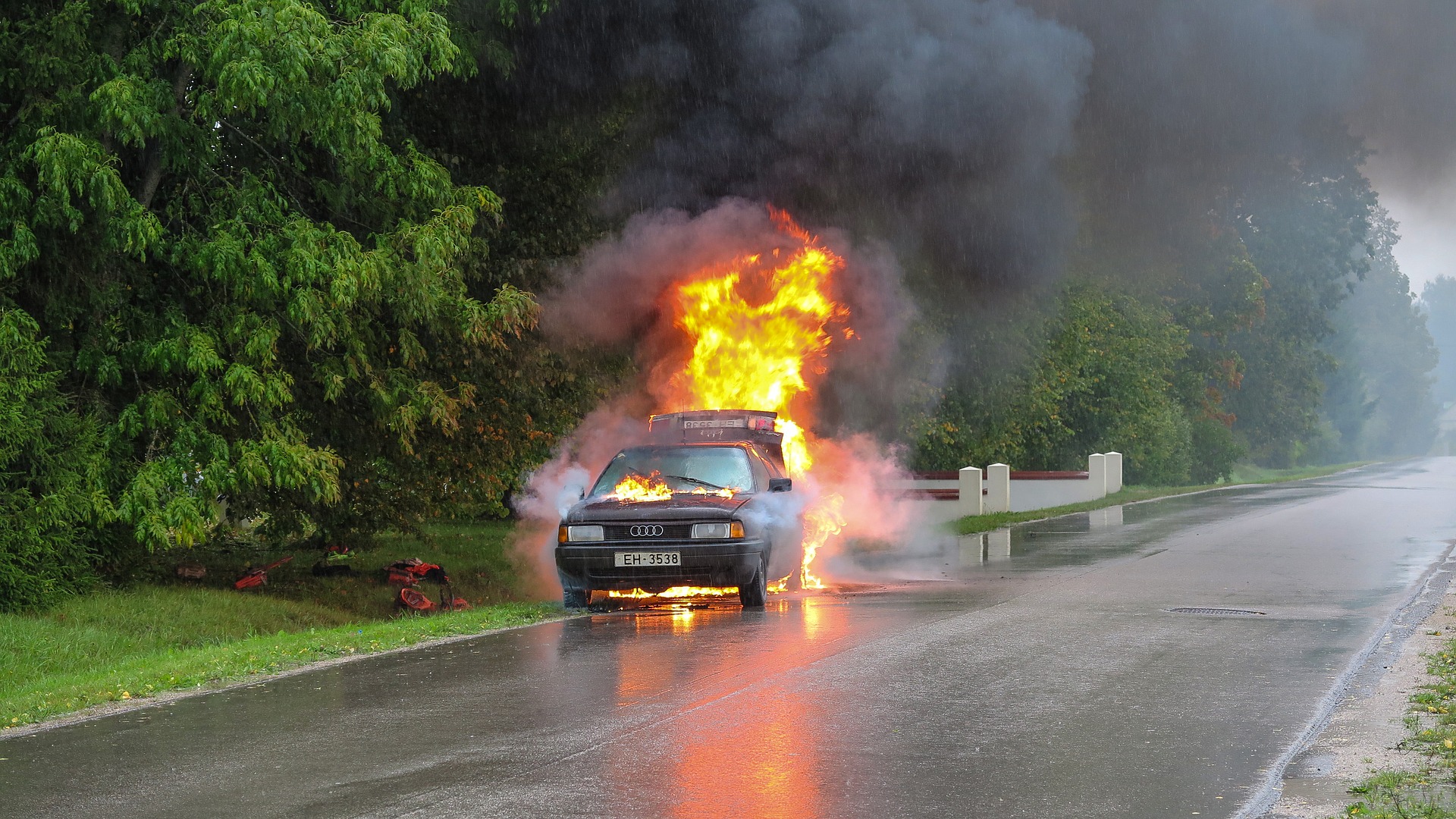 A car is on fie on an empty street in the rain