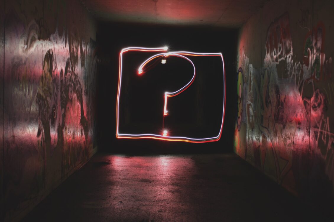 A question mark drawn in neon on a dark background